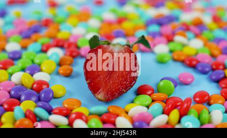 Strawberry among colorful sweet candy on blue pastel background. Stock Photo