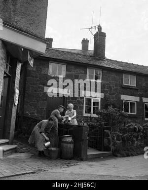 A village without water at Ruyton-XI-Towns, Shropshire. Churns are placed outside each house and are filled with ten gallons of water twice a week from a water cart. To augment their ration of churn water villagers place baths and other receptacles under drainpipes to catch water for washing and bathing. John Beegles, 74, getting water from the churn outside his house for his 74-year-old wife Alice. His next door neighbour, Mrs Betty Guyatt, 31, also takes her share. 31st August 1956. Stock Photo