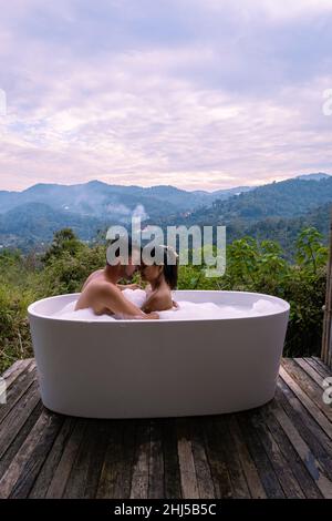 Bathtub during sunset in the mountains of Chiang Mai Thailand, relaxing in outdoor wood fire hot tub out in the wilderness. relaxing bath, couple man and woman in bathtub Stock Photo
