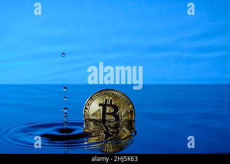 Splash water from a falling raindrops and a bitcoin coin in the water against the blue sky Stock Photo