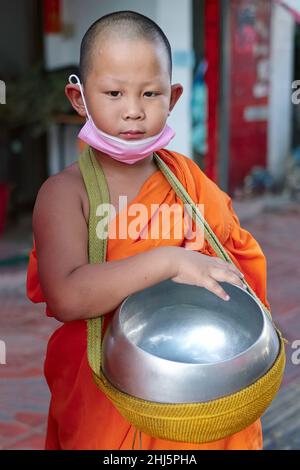 A young, 8 yr old child monk or novice during the traditional monks' alms round, performed early morning, carrying his alms bowl; Bangkok, Thailand Stock Photo