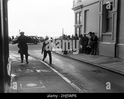 Brighton catches the full force of the gale. Visitors on the seafront find themselves trapped by terrific gusts which make them cling to any support they can find. 29th July 1956. Stock Photo
