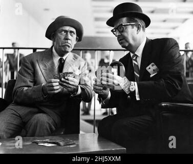 Phil Silvers, famous as Master Sergeant Ernest G. Bilko on the Phil Silvers television show, enjoys a game of cards with comedian Tommy Trinder (left) in the lounge at Heathrow Airport after he arrived in London with his wife Evelyn. 15th June 1959. Stock Photo