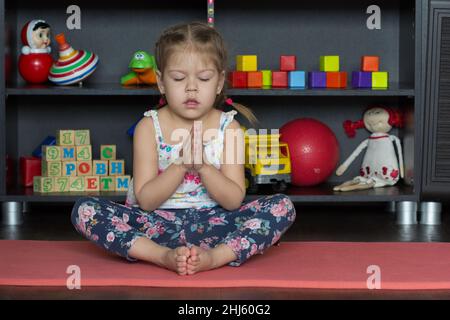 Little girl making yoga pose of cobbler or butterfly as sit on buttocks with tall spine, bend legs, place soles of feet together, and gently flap legs Stock Photo