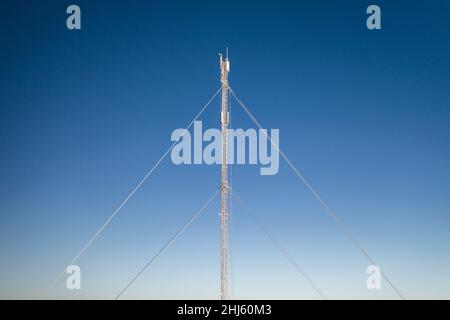 Frost covered telecommunications mast against blue sky in winter. Stock Photo