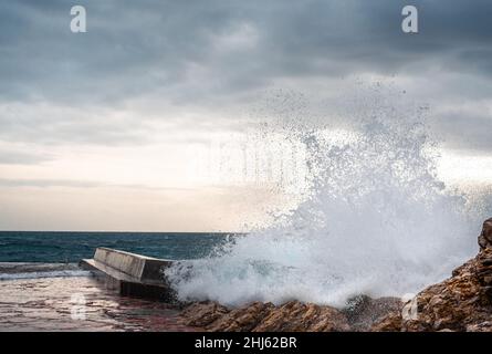Big wave splash on pier. Big sea wave on a windy day. Waves crash against concrete breakwater at port entrance. Giant waves breaking on the breakwater Stock Photo