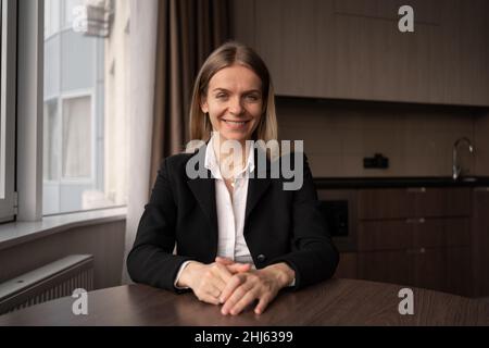 Smiling young woman blogger, caucasian influencer, sitting at table, looking at camera, making video conference, vlogger girl filming blog at home Stock Photo