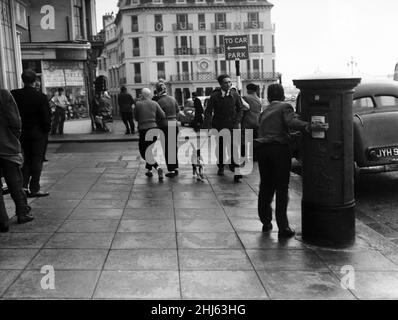 Brighton catches the full force of the gale. Visitors on the seafront find themselves trapped by terrific gusts which make them cling to any support they can find. 29th July 1956. Stock Photo