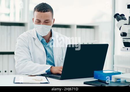 Not your average drug trial. Shot of a young scientist using a laptop while working on a coronavirus cure in a laboratory. Stock Photo