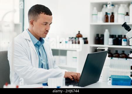 Keep calm, the cure is coming. Shot of a young scientist using a laptop while working in a laboratory. Stock Photo