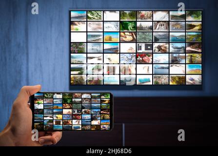 Television streaming, TV broadcast. a man with a phone in his hand and a TV with same image on the screens. cross-platform. Multimedia streaming VoD c Stock Photo