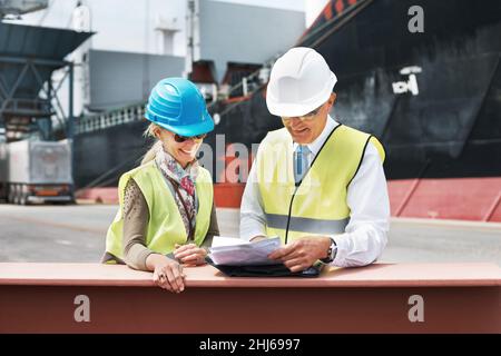New business ventures are always exciting. Two dock workers holding paperwork while standing in the shipyard. Stock Photo