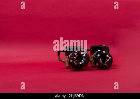 Two doughnuts in front of two mugs on a crimson background Stock Photo