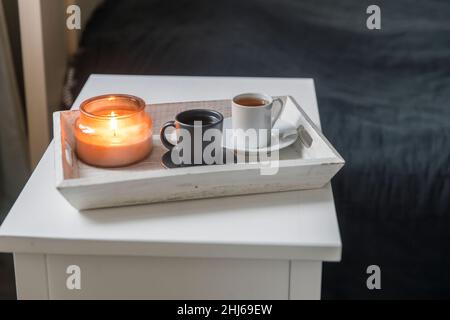 A two cups of coffee: white and black on a tray and a candlestick are on the bedside table Stock Photo