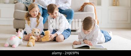 Happy young caucasian family resting in a new cozy design home on weekends. Delighted parents resting in their own home, children have fun sitting on the floor with toys and a book Stock Photo