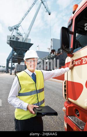 Transportation ensures successful trade. Portrait of a dock worker standing at the harbor amidst shipping industry activity. Stock Photo