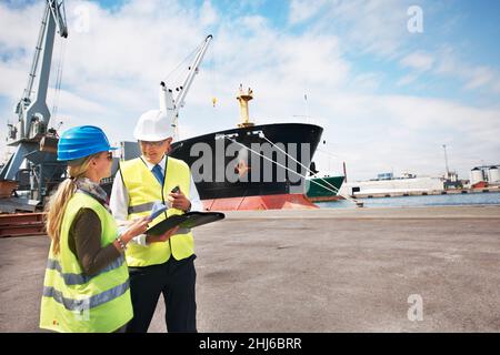Open communication brings results. Two dock workers holding paperwork while standing in the shipyard. Stock Photo
