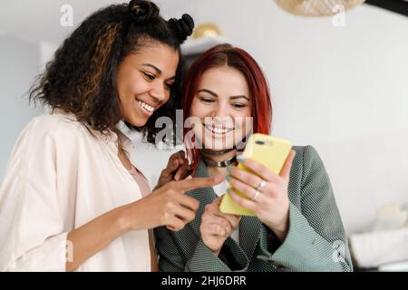 Young multiracial two women smiling while using mobile phone at home Stock Photo