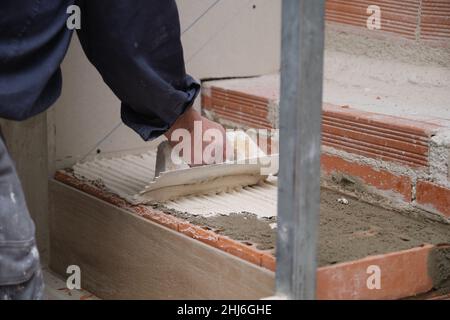 Unrecognizable bricklayer using a notched trowel to build a staircase in a home. Stock Photo