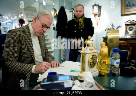 Amsterdam , Netherlands. Antique Clock's Store owner writing invoices for a fresh customer after they bought  a 350 year old clock and hour work. Stock Photo
