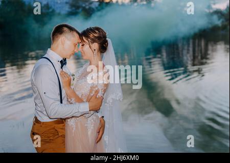 Bride and groom with the blue and yellow colored smoke bombs in the summer park. The bride and groom with the colored smoke at the background of Stock Photo