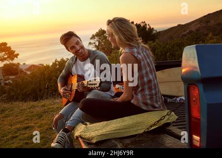 Songs from the heart. Shot of a young man playing guitar for his girlfriend on a roadtrip. Stock Photo