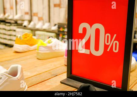 20 sales sign card in clothes store close-up across shelves with shoes and sneakers. Sales, discount, black Friday, cyber Monday, season sales concept Stock Photo