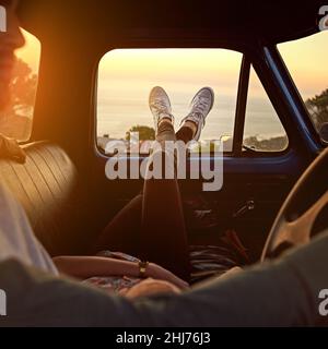 Take a break, you deserve it. Shot of a young woman relaxing on her boyfriends lap with her feet up during a road trip. Stock Photo