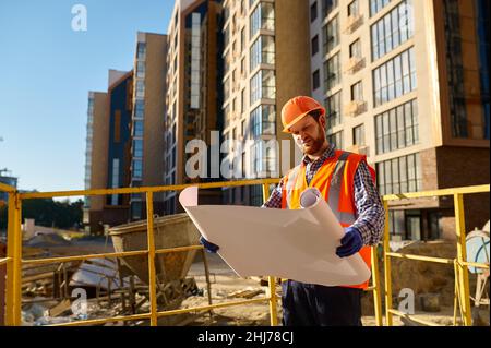 Builder or engineer holding blueprint standing outside Stock Photo
