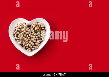 Uncooked assorted legumes in heart shape plate on red background Stock Photo