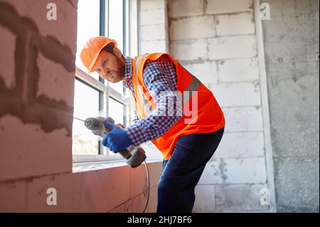 Builder in hardhat working with drill indoors Stock Photo