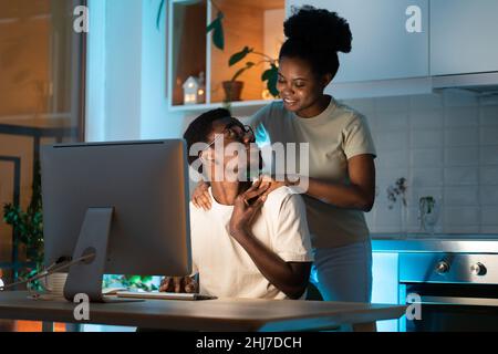 Woman hugging husband from behind while he working on computer remotely from home late at night Stock Photo