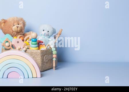 Toy box full of baby kid toys. Container with teddy bear, wooden rattles, stacking pyramid and wood blocks on light blue background. Cute toys Stock Photo
