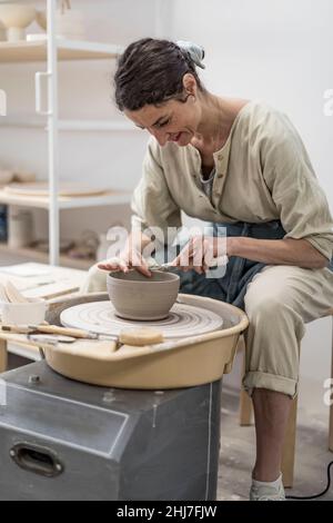 Female potter modeling clay bowl in workshop - Artisan work and creative craft concept Stock Photo