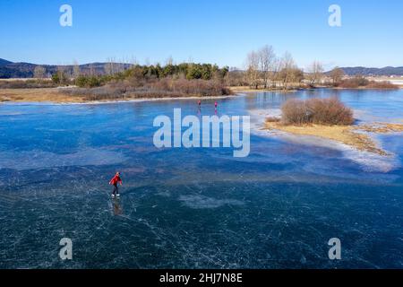 Aerial view of a woman ice skating on frozen intermittent lake Cerknica, Slovenia on a sunny day Stock Photo