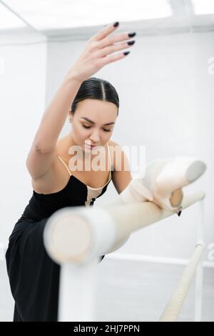 young ballerina stretching at barre in studio on blurred foreground Stock Photo