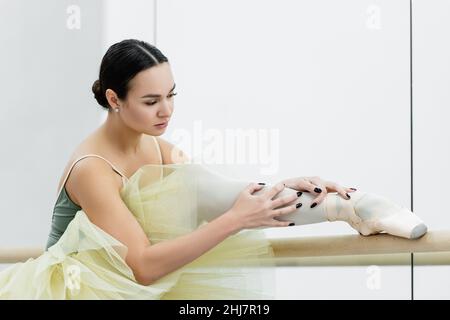 young ballerina stretching leg while training in dancing hall Stock Photo
