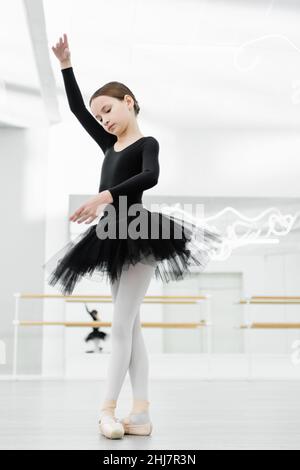 slim girl in black tutu dancing with raised hand in ballet studio Stock Photo