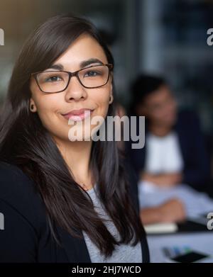 She's an asset to the company. Portrait of a smiling young businesswoman in an office with colleagues in the background. Stock Photo