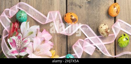 banner with multicolored alstroemeria, pink, yellow, magenta, white and red alstroemerias with painted quail eggs. background from multi-colored flowers and painted eggs with pink ribbon on wooden table.Top view Stock Photo