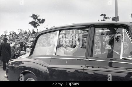1977, historical, happy faces and union jack flags as Her Majesty, Queen Elizabeth II and Prince Philip sitting in her official state vehicle, a Rolls-Royce Phanton VI, wave to the crowds at the roadside, London, England, UK during the Silver Jubliee celebrations. Stock Photo