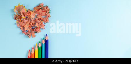 banner with Sharpened colored pencils and heart-shaped pencil shavings on pastel blue color. Rainbow or LGBT pencils. Decoration for St. Valentine's Day. Top view