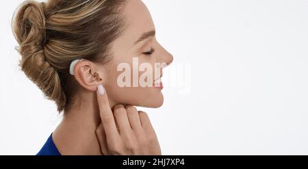 Positive woman with hearing aid behind her ear enjoying her hearing restoration, isolated on white. Hearing aids Stock Photo