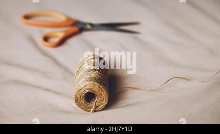 On the beige fabric there are scissors for cutting and a coil of hemp rope. Accessories for the tailor's work. Handmade work. Household items. Stock Photo