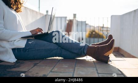 Unrecognizable young woman working with her computer sitting on the floor in the terrace Stock Photo