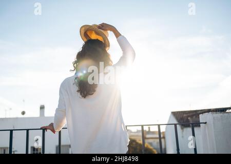 Unrecognizable young woman taking off her hat on a sunny day on the rooftop Stock Photo