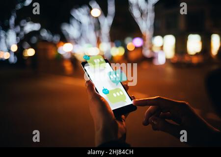 User dialogue with AI chat bot on futuristic smartphone interface, while walking along the city street, close-up Stock Photo