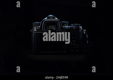 Low key light, Backside of a DSLR with black body in a black background, showing the LCD turned off, with a rim light on the body of the camera. Stock Photo