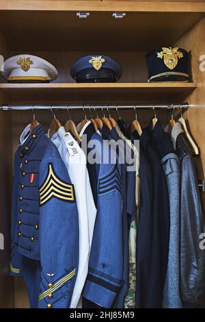 Clothing made for combat. Shot of various military jackets and hats hanging in a closet. Stock Photo