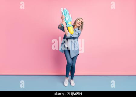 Full body photo of cool aged lady go hold gun wear jeans shirt isolated on pink background Stock Photo